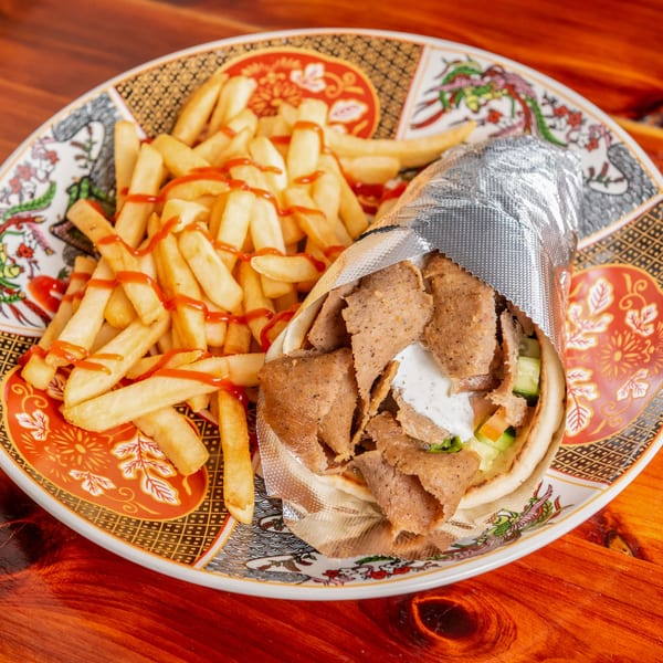 Gyro wrapped in foil with fries drizzled with ketchup on a decorative plate.