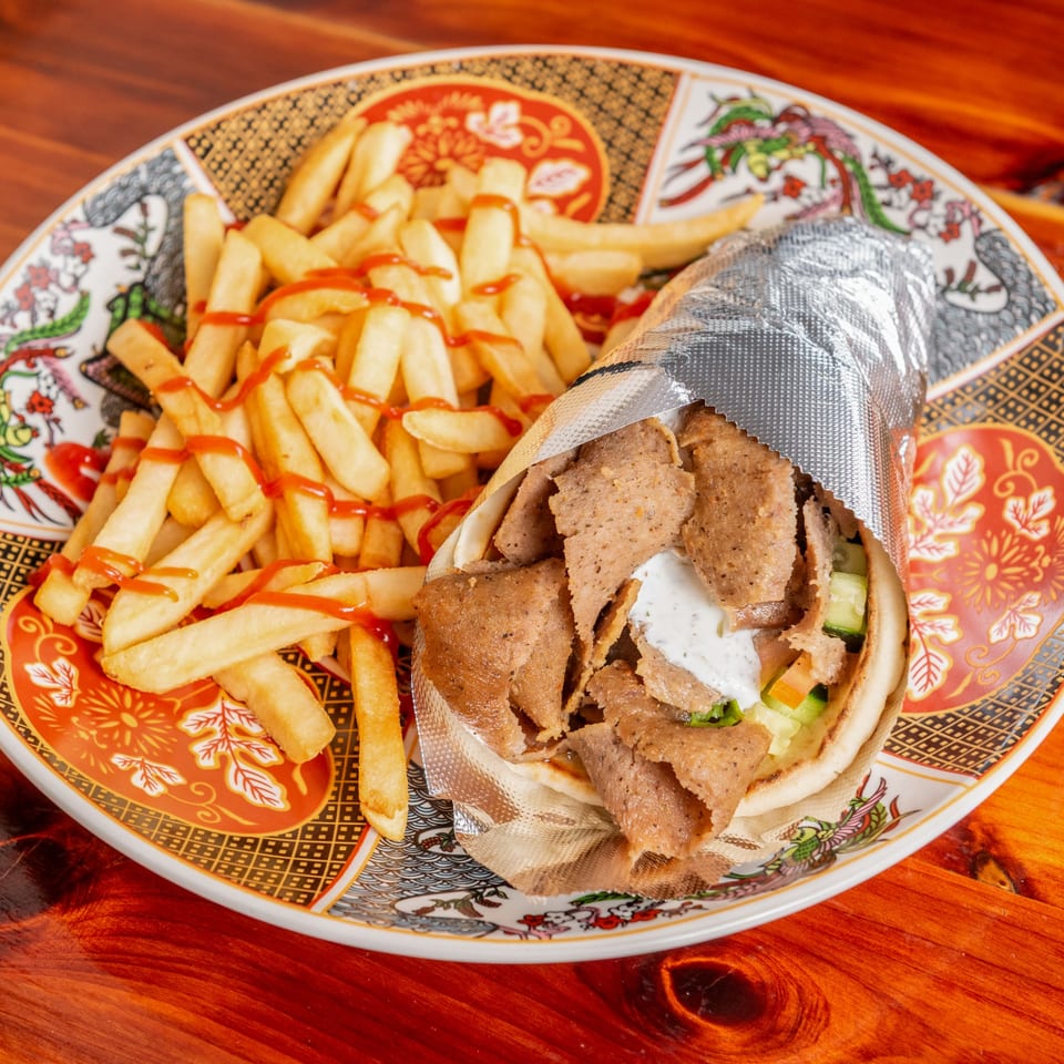 Gyro wrapped in foil with fries drizzled with ketchup on a decorative plate.