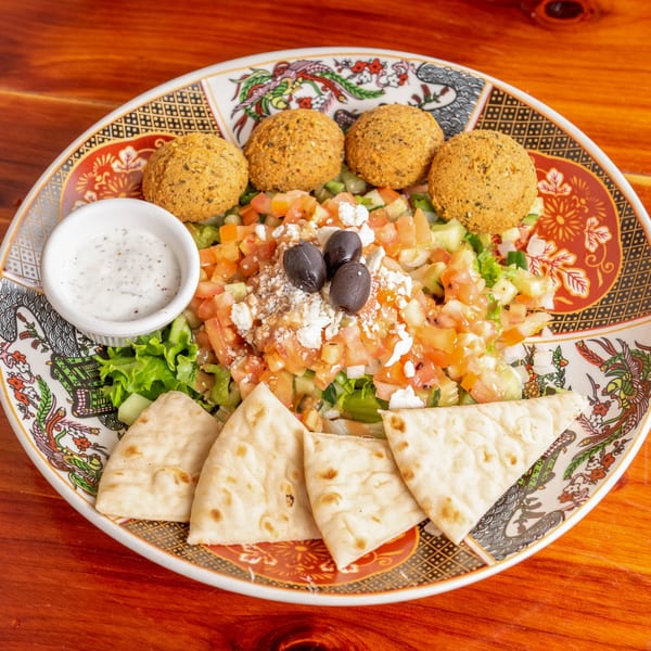 Falafel plate with salad, olives, feta, pita bread, and a side of white sauce.