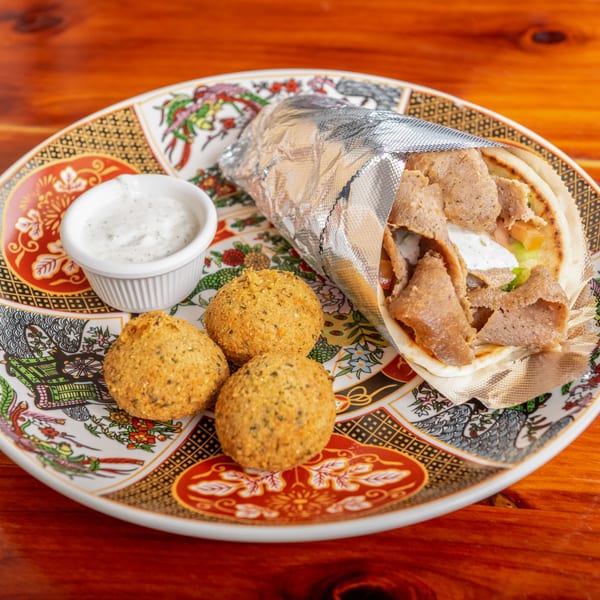Gyro wrap with meat, sauce, and vegetables, served with falafel balls and a side of white sauce.